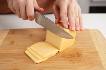 Woman cutting cheese in the kitchen, slicing cheddar on a wooden board, dairy product preparation