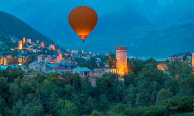 Hot air balloon flying over mountain village with ancient towers at dusk - Mestia, Svaneti, Georgia