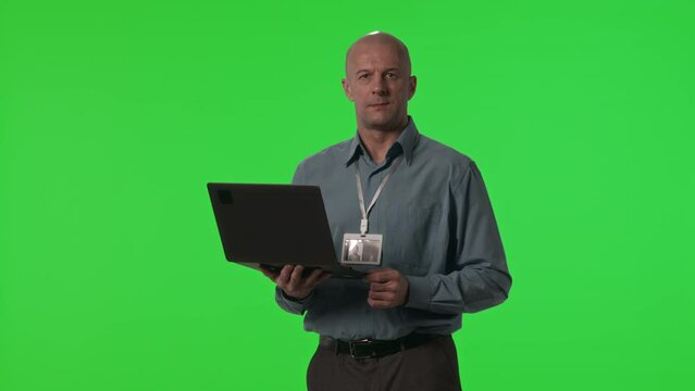 Portrait of data center engineer wearing badge holding laptop and posing for camera against green chroma key background in studio