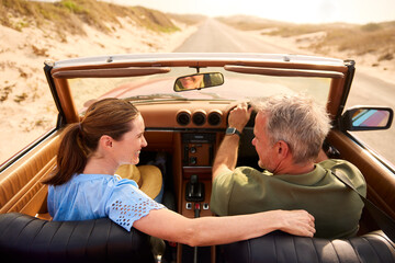 Retired Senior Couple On Vacation Driving In Classic Sports Car On Road Trip Through Countryside