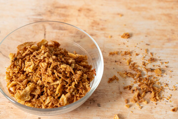 Crispy fried golden onions flakes in a glass bowl on a wooden surface used for garnishing