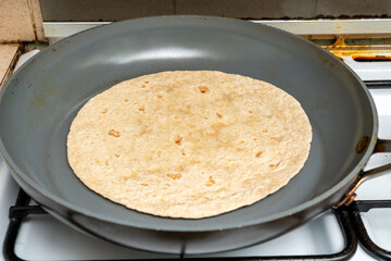 Round Indian flat bread, roti or chapati made from unleavened dough cooking in a non-stick frying pan.