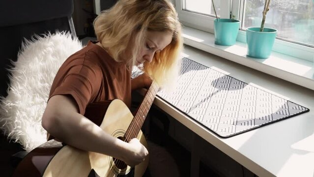 Woman playing guitar at home, acoustic music, hobbyist musician, cozy atmosphere
