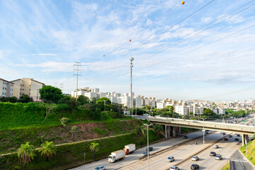 Car and truck traffic on an important avenue in the city of Belo Horizonte. Buildings, bridge and highway. Blue sky with clouds. Trees. Power poles. Horizontal.