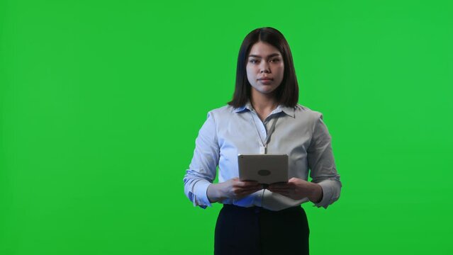Portrait of female data center worker holding digital tablet, turning to camera and posing against chroma key green background in studio