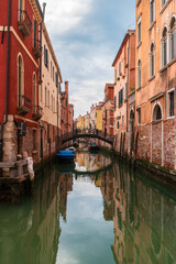 View of quiet street with old bridge and narrow canal with boats along brink. The residential area of Venice, Italy.