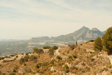Film style photography of a landscape in Alicante, Spain. It features a foggy day with the mountains and the mediterranean sea in the background, with a dry landscape and a hiking trail.