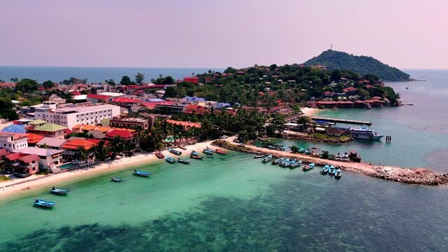 Aerial view of Haad Rin District and Haad Rin Pier (Haad Rin Queen Ferry), Koh Phangan, Thailand. Drone travelling from the sea towards the beach. 
