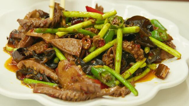 Graded UHD closeup shot of the delicious Chinese food. Squid stir-fried with garlic arrows, mushrooms and red hot peppers in a soy sauce. Filmed as 6k RAW.