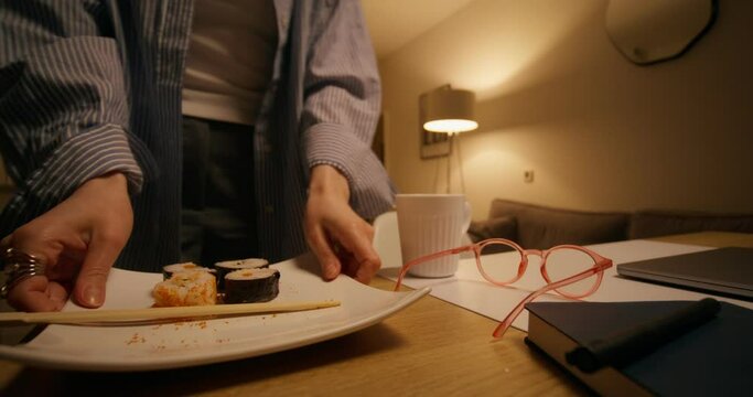 The woman closes the laptop and removes the plate from the desktop, ending the working day at home