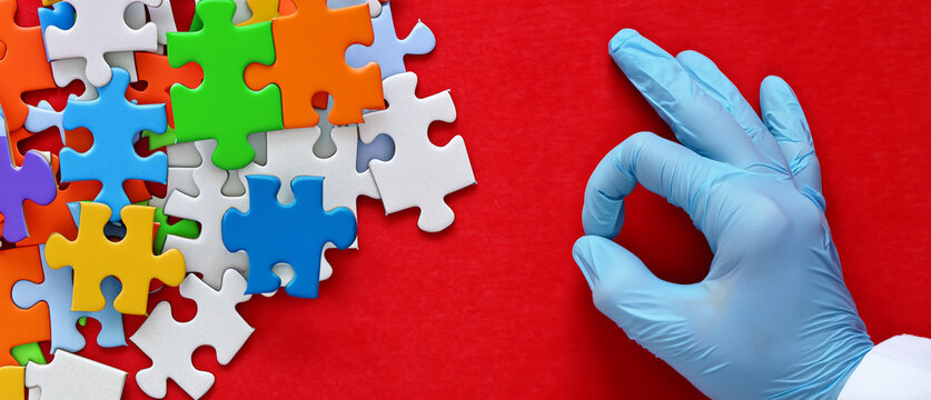 Scientist or physician, health care practitioner's hand in blue surgical glove picking up a piece of jigsaw puzzle on red background, metaphor about making the good choice in a complex situation