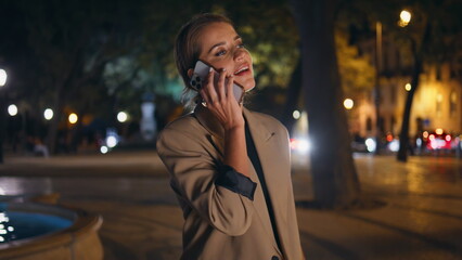 Fashionable woman answering call on night street. Relaxed businesswoman speaking - Powered by Adobe