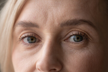 A close-up view captures the top half of a womans face, revealing her striking blue eyes, soft...