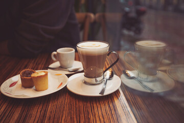 Coffee cup with sweets on the table of cafe. Coffee latte on the wood desk in coffee shop cafe restuarant,Italy. Brake time with a mug of coffee and city view though window. 