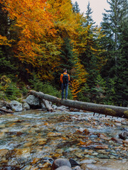 Man on a log over the river in autumnal forest. Mountain river and hiker traveller