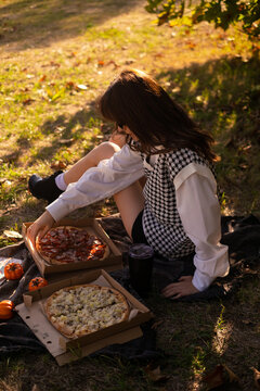 A woman enjoys a spring picnic in the park, savoring pizza on a warm day, depicting outdoor weekend leisure and promoting a pizzeria.