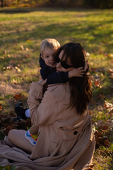 A mother and son embrace and play in the spring park. The boy holds green tree leaves while the...