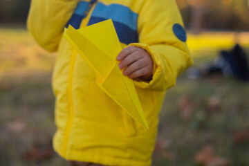 A blond boy plays with paper airplanes in the park, radiating joy and excitement during outdoor weekend fun. It's a perfect family getaway filled with laughter and enjoyment.