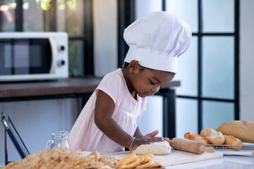 Happy little African girl wear chef hat in bakery kitchen, she learned about baking