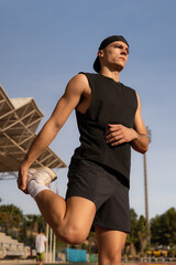 Young male athlete warming up his legs and stretching. Preparing for competition in a sports facility. Vertical photo
