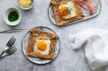 Homemade buckwheat crepes. Galettes Bretonnes with cheese, fried egg and ham on a grey background. Traditional French cuisine.