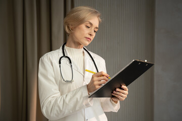 A seasoned medical professional stands focused on examining patient charts, with a pen poised for...