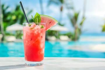 Watermelon lemonade in a glass on a white concrete surface against the background of a luxury tropical hotel