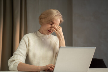 A woman in a white turtleneck sweater shows signs of stress or fatigue as she pauses from her work...