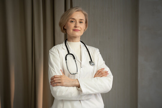 A professional female doctor stands confidently with her arms crossed in a medical clinic, wearing a white lab coat and stethoscope, with a warm and reassuring smile, suggesting an atmosphere of trust