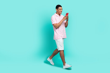 Fototapeta na wymiar Full size photo of nice guy dressed casual polo white shorts read sms on smartphone walk to empty space isolated on teal color background