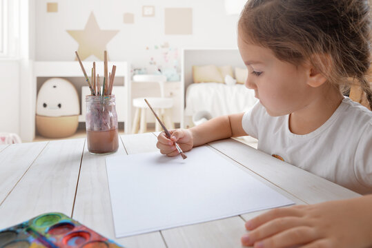 Young girl painting with watercolors on white paper in her room. Ideal for children's creativity or artistic concepts