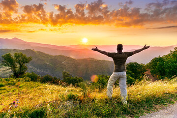 rejoicing man with beautiful scenic mountain sunset landscape on background. happy man watching...