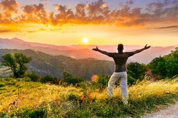 rejoicing man with beautiful scenic mountain sunset landscape on background. happy man watching amazing evening sunset