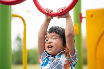 Obraz premium Adorable preschool boy enjoying bar lifting in outdoor playground in city park