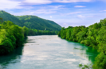 Fototapeta premium beautiful landscape of spring or summer sunset river with blue water and green hills on sides and mountains with amazing cloude sky on background