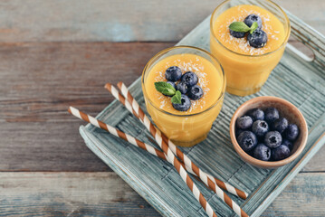 Refreshing and healthy mango smoothie in glasses with coconut flakes and fresh blueberries - 764037374