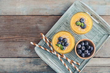 Refreshing and healthy mango smoothie in glasses with coconut flakes and fresh blueberries - 764037380