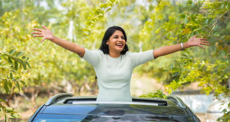 Fototapeta premium Happy woman feeling nature fresh air by stretching arms on car sunroof - concept of freedom, traveller and refreshment