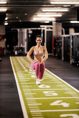 A fit sportswoman is practicing lunges in a gym.
