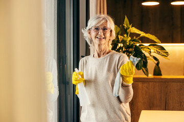 A tidy senior woman is holding detergent and doing chores at home.