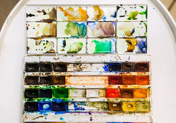 Background, texture of watercolor colored paints in disarray, in a dirty box on a white table. Photography, creativity concept, top view.