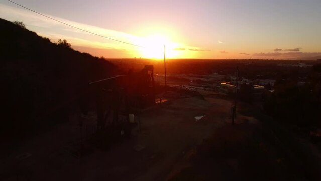 Aerial: Drone Forward Shot Of Oil Pumping Jack On Hill In City During Sunset - Culver City, California