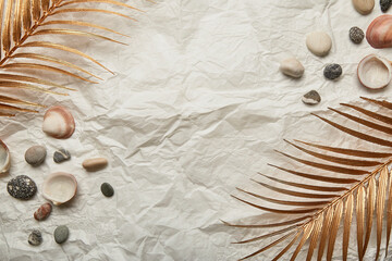 golden palm leaf, pebbles and seashells on summer background with copy space.