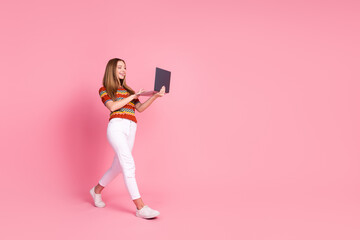 Full size profile photo of nice cheerful girl walking hold use laptop empty space isolated on pink color background