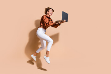 Fototapeta na wymiar Full length photo of positive pretty lady dressed brown top jumping texting modern gadget empty space isolated beige color background