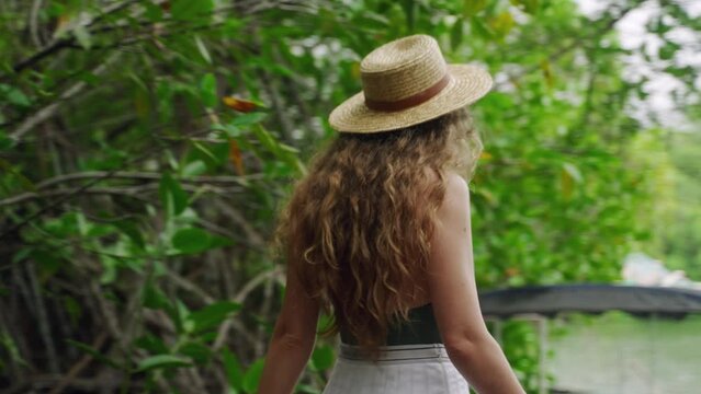 Woman in straw hat boards boat on lake for leisurely cruise. Nature enthusiast explores wetlands, embarks on eco tour. Solo traveler enjoys serene water excursion, seeks adventure, relaxation. Slowmo
