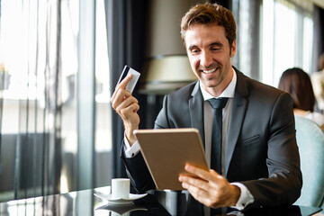Successful handsome business man holding credit card, using digital tablet. Online shopping concept