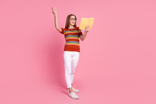 Full size photo of excited cheerful girl read book raise hand empty space ad isolated on pink color background