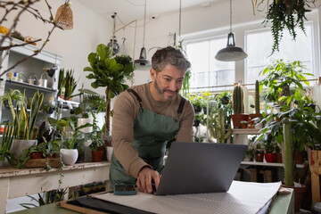 Hispanic male using a laptop computer in his small business plant store