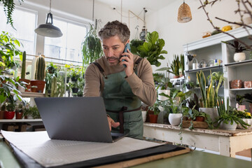Plant shop owner using a laptop computer and smartphone in gas store for electronic banking
